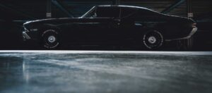 Classic black muscle car parked in garage with hood up